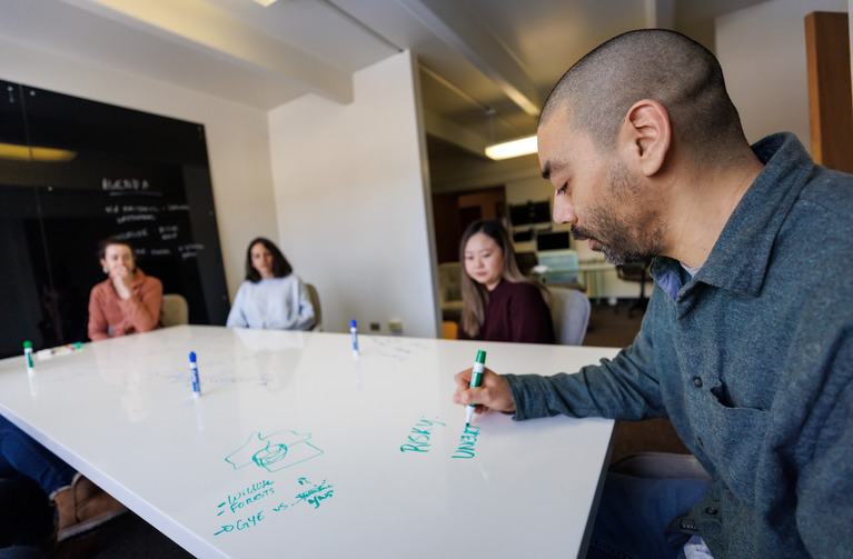 people discussing and writing around a whiteboard table