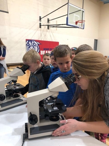 Mercedes helping a student adjust the focus of a microscope