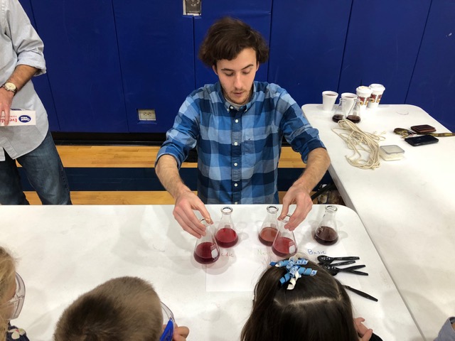 Tyler lining up erlenmeyer flasks for students to compare differences in the color of the liquid in each