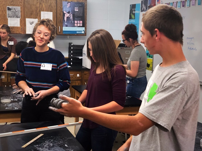 Brenna talking with students as they perform an experiment with clay