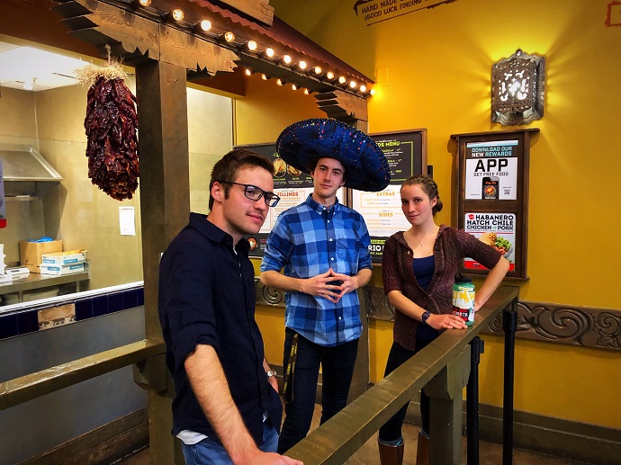 Brett, Tyler (who is wearing a sombrero), and Ella pose for the camera in a restaurant 