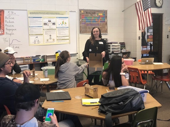 Olivia talking at the front of the classroom holding a box