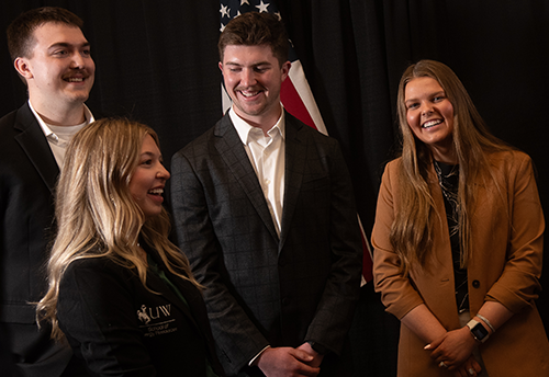 students dressed in workwear smiling and talking in front of an American flag