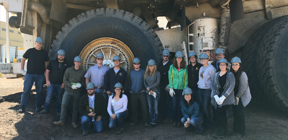 Students in front of the giant wheels of a coal mine haul truck