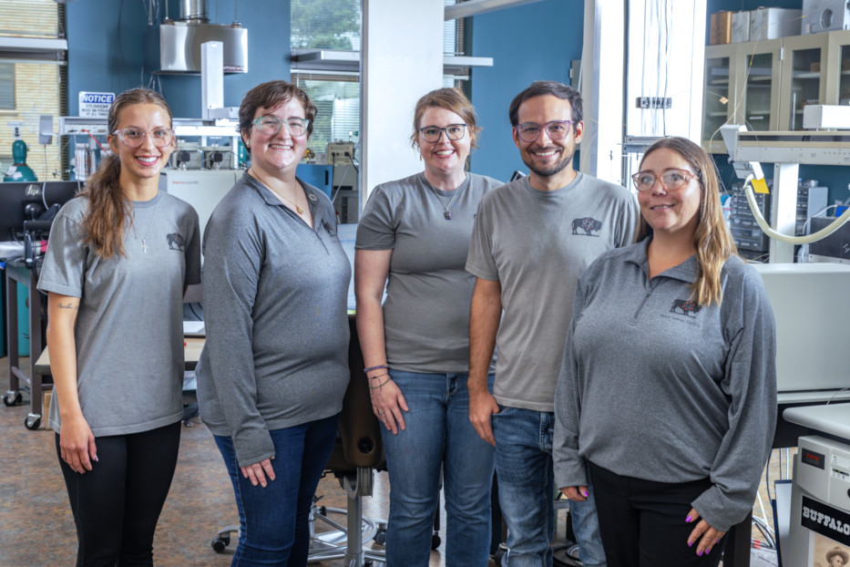 5 lab technicians standing in a lab in front of instruments.