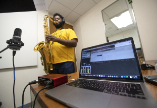 A person playing the saxophone while a computer records the audio.