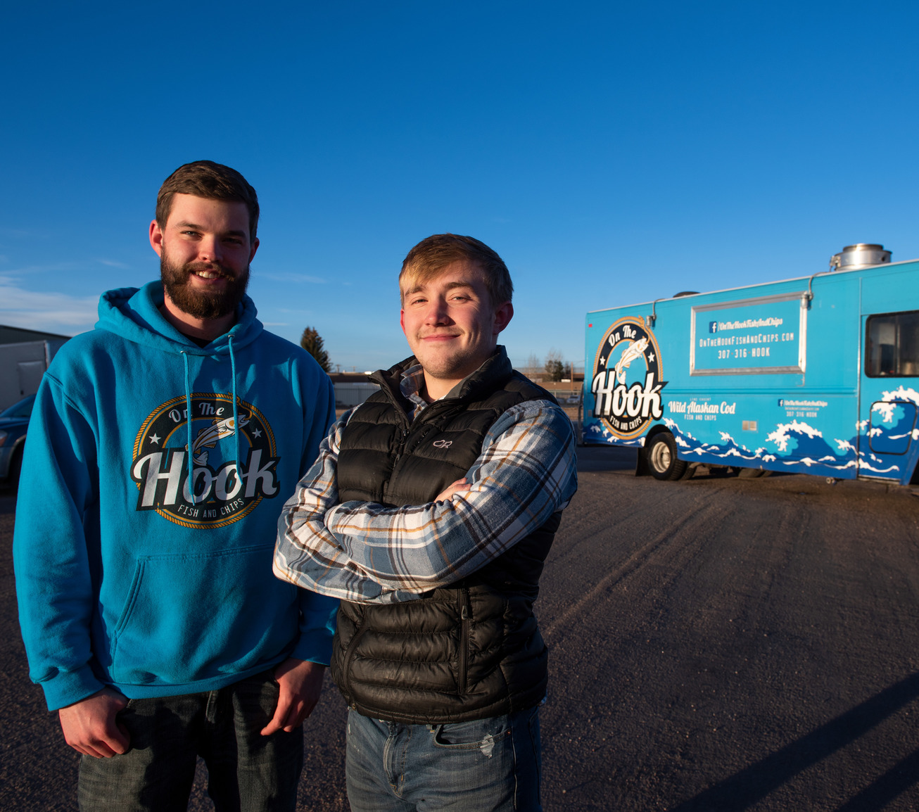 Two former UW students pose in front of their On the Hook food truck.