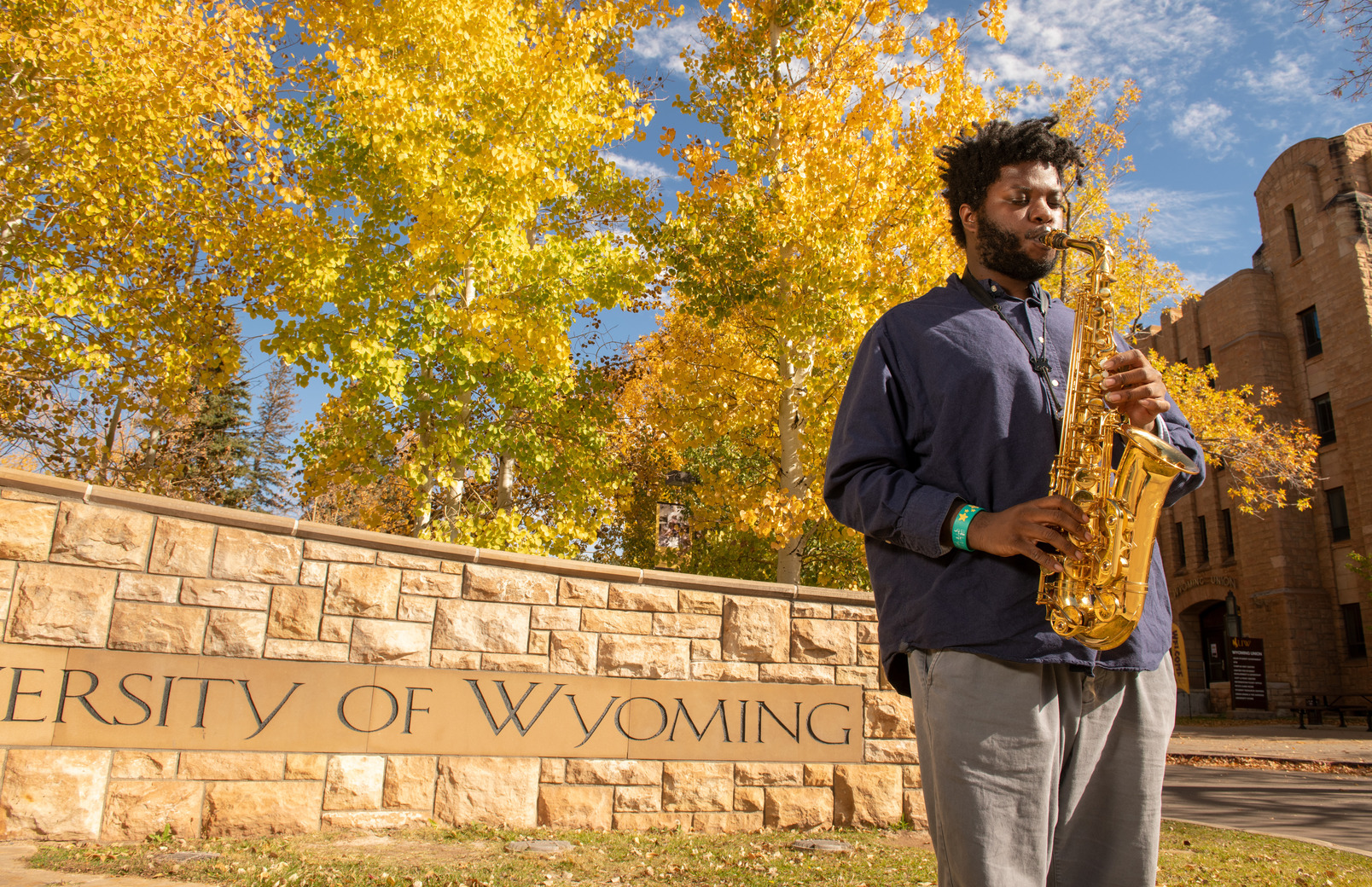 Student playing saxophone outside of "University of Wyoming" sign