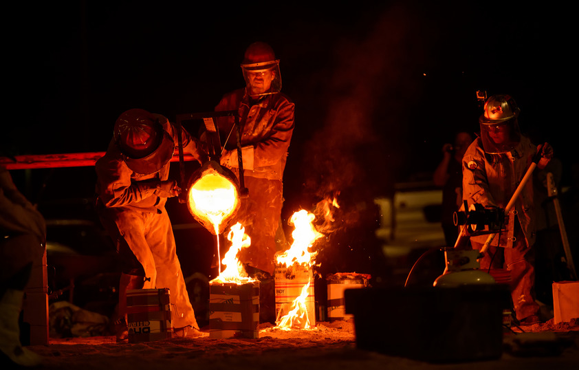 Professors and students outside in the dark pouring molten iron into flaming molds
