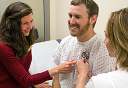 two women use a stethoscope on a man