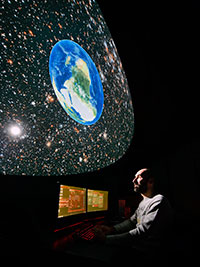 man at planetrium control board with star field displayed above him