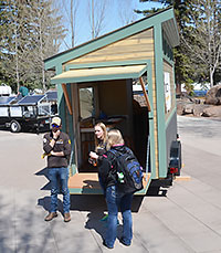three people standing in front of a tiny house on a trailer, open at the back