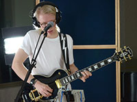 man playing electric guitar behind a microphone while wearing headphones