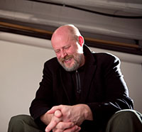 man sitting and smiling with hands clasped in front of him
