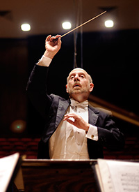 man in white tie and tails with baton raised conducting an orchestra
