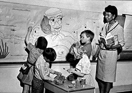 woman with four children beside a classroom bulletin board