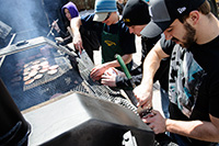 people flipping hamburgers on a line of grills outdoors
