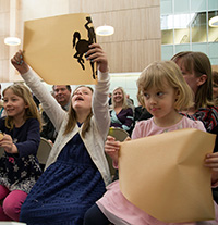 little girls  holding up sections of very wide ribbon with bucking horses on it