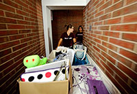 young woman pushing cart of belongings in brick hallway