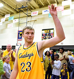 man in gold basketball uniform waving with people behind him