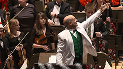 man in white suit and green vest  conducting orchestra, arm upraised