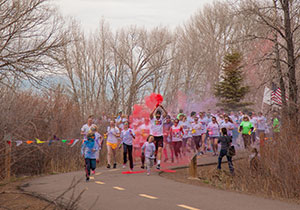 people running on a path with clouds of color in the air above them