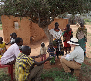 woman sitting under a tree with a group of people in an African village