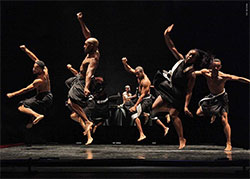 group of shirtless people dancing animatedly in unison on a stage
