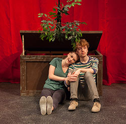 man and woman sitting on stage floor, leaning against a box