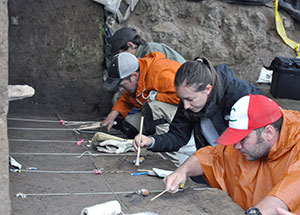 four people kneeling and carefully excavating an area in front of them