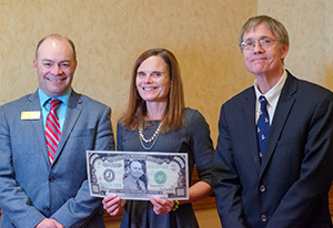 two men and a woman, with the woman holding up an award made to look a little like US currency