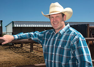 man in cowboy hat standing with arm on metal fence