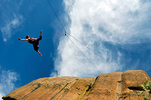 person suspended by wires in front of a rock face