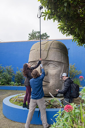 a woman and two men photograph a large stone head