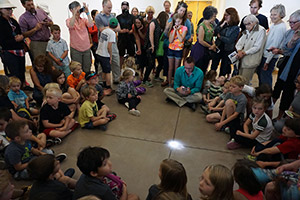 group of people, mostly children, gathered around a spot of light on the floor