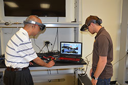 two men wearing augmented reality goggles look at computer