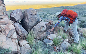 man bending over to study rocks on hillside