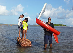 two children and a man pose with a small sailboat