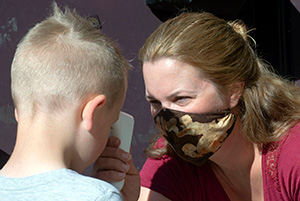 woman in facemask taking temperature of small child