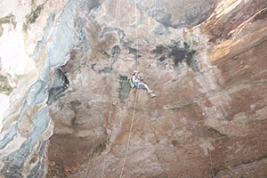 person suspended on lines going down into cave