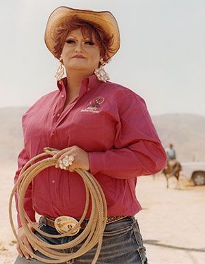 older woman in cowboy hat and heavy jewelry holding a coiled lasso