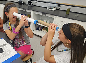 two girls looking at each other through homemade telescopes