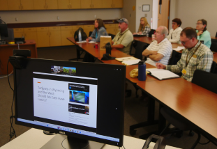 a computer screen with a presentation and people sitting at tables in the background