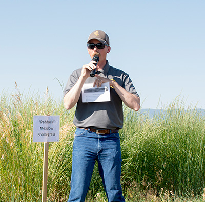 Brian Mealor speaking into a microphone in front of a grass research plot