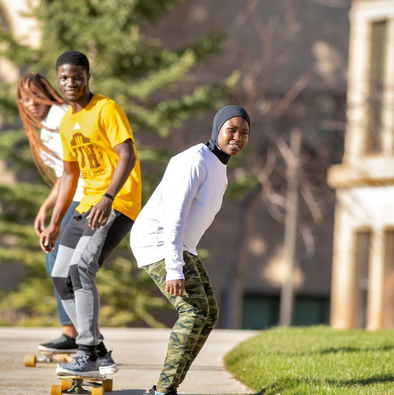 Three students skateboarding on campus. 