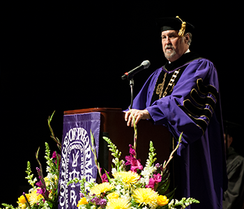 man in cap and gown speaking at podium