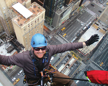 man in climbing gear dangling above a city street