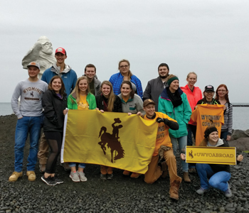 group of people on a rocky beach with a UW flag
