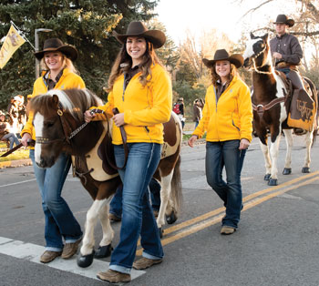 women leading a pony in a parade with a man on a horse behind them