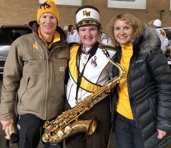 three people, one in a band uniform holding a saxophone
